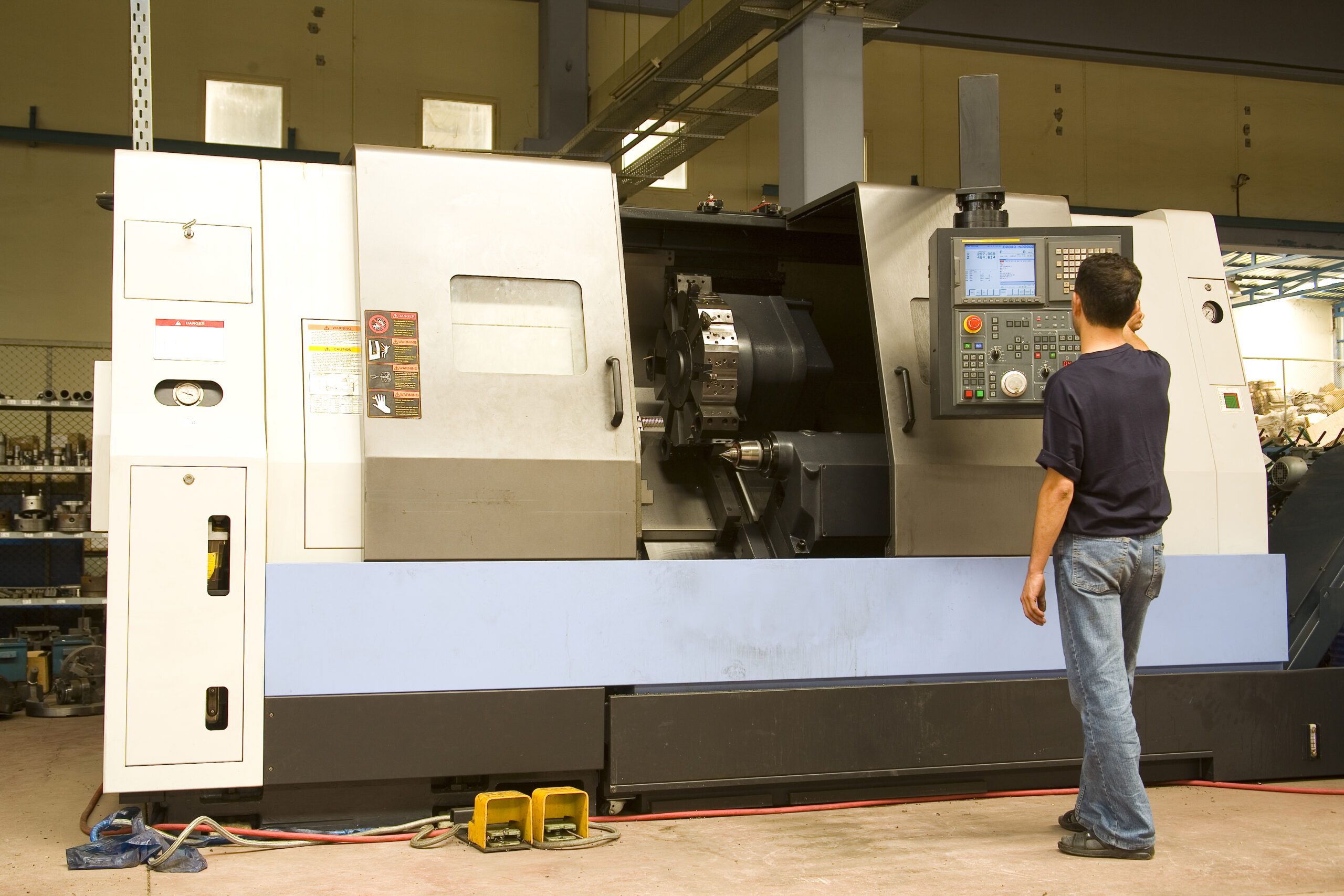 A technician operates a CNC lathe machine in a workshop, focusing on the control panel to adjust settings for precision machining tasks.